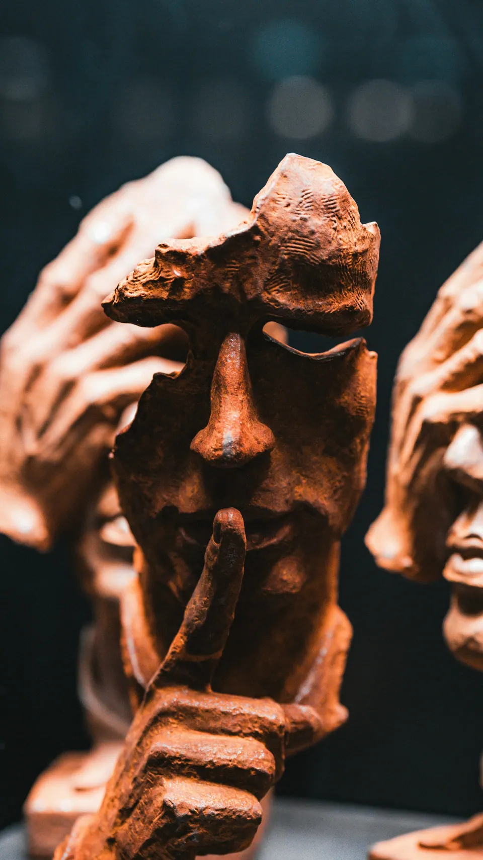 Escultura de barro com o dedo sobre os lábios pedindo silêncio, entre mãos que cobrem o rosto