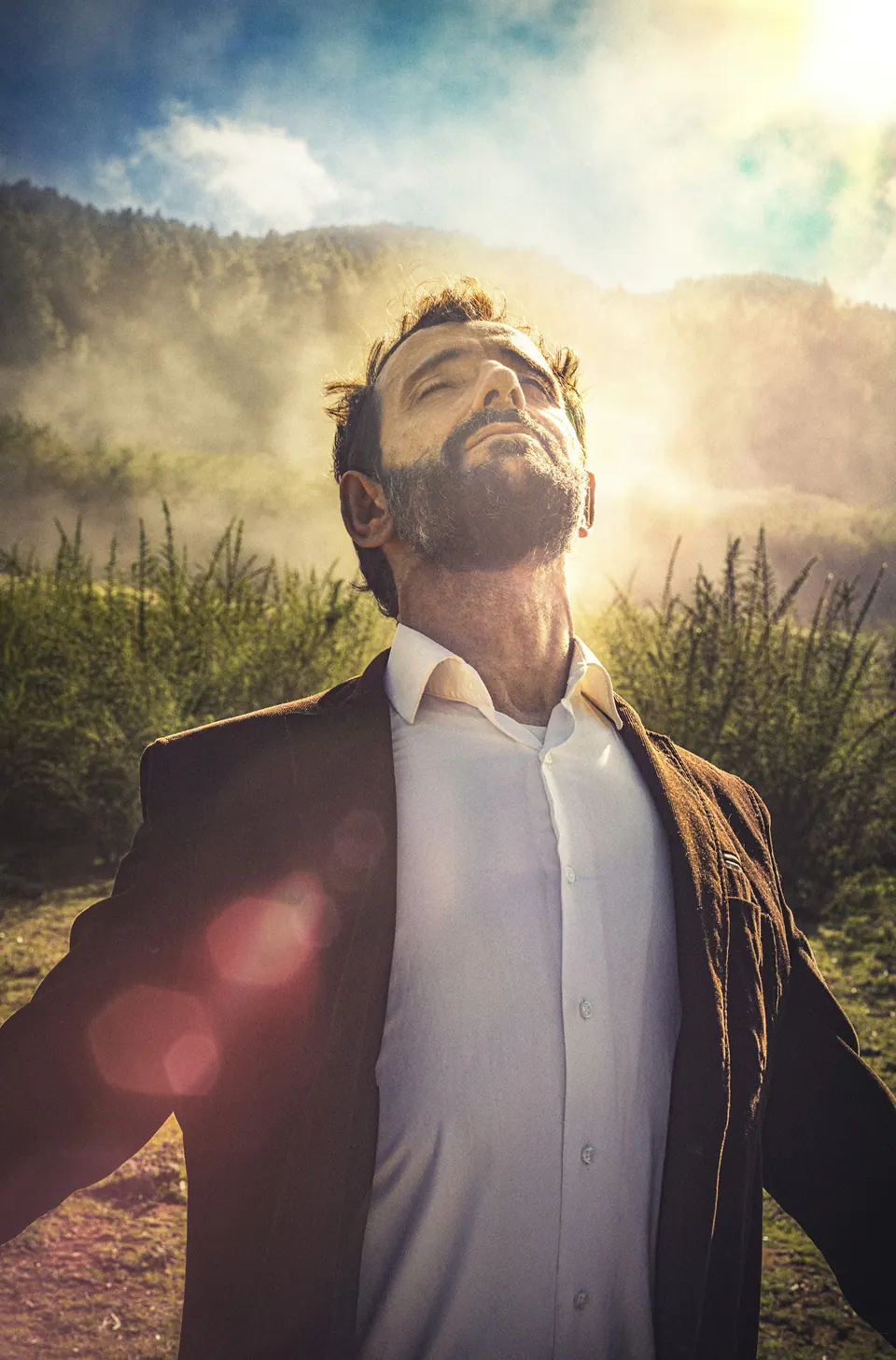 Homem de braços abertos ao sol, de olhos fechados, num campo