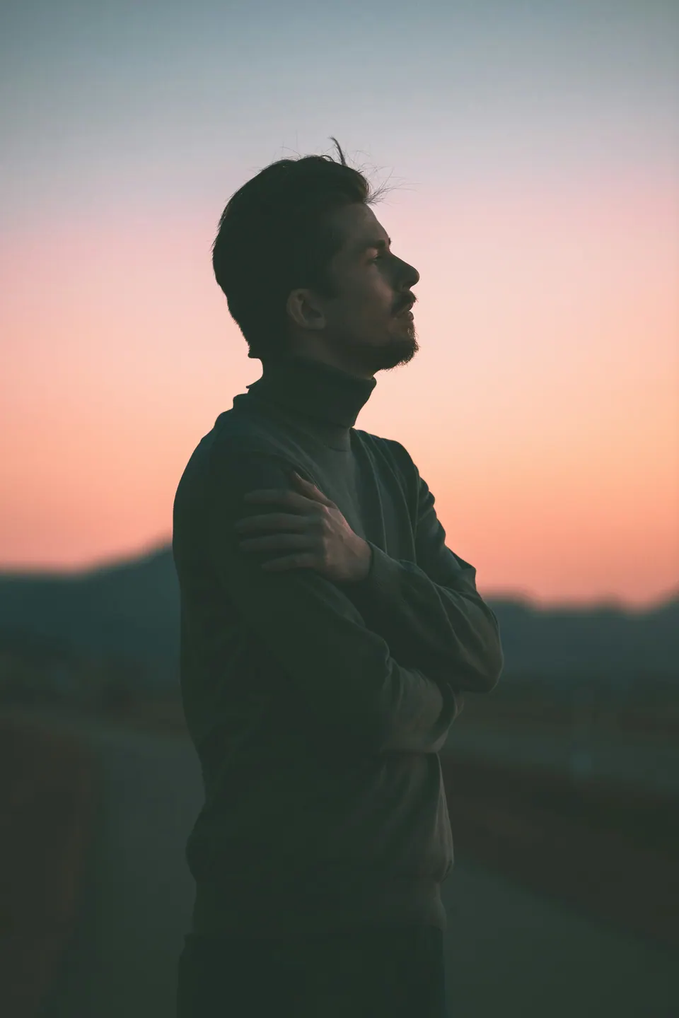 Homem de perfil ao pôr do sol, de braços cruzados, olhando o horizonte